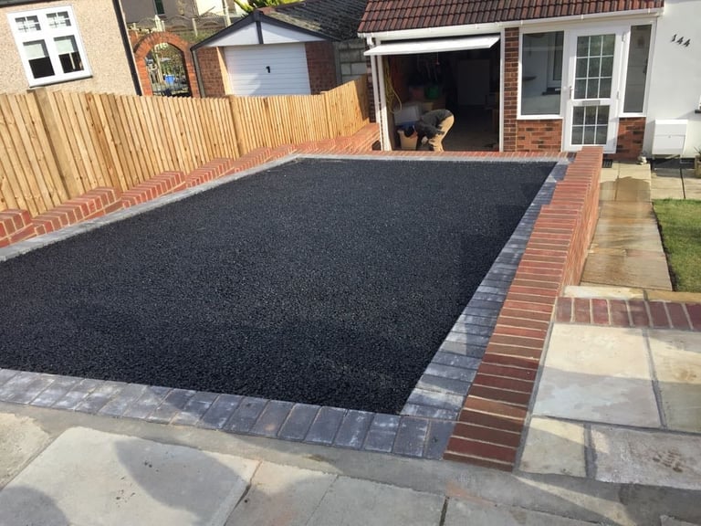 Newly constructed driveway with dark asphalt surface bordered by red brick edging in a residential backyard