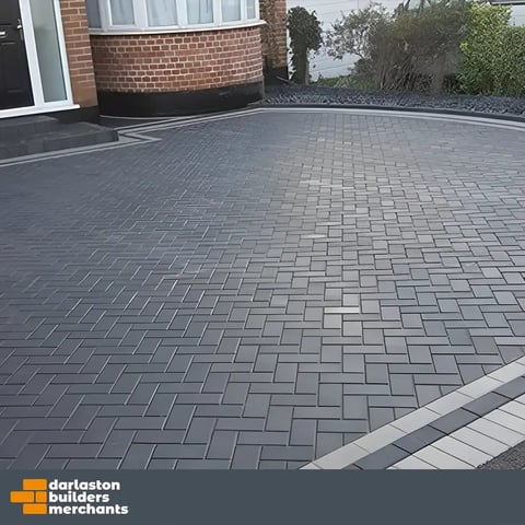 Modern driveway with gray herringbone patterned pavers, brick home foundation, and landscaping borders