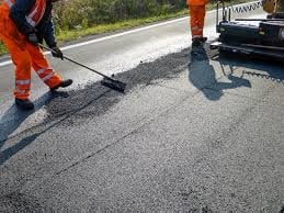 Worker in orange safety gear using equipment to smooth asphalt on a road construction site