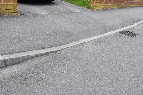 Residential driveway with curved curbing, red brick pillars, and manicured lawn visible in background