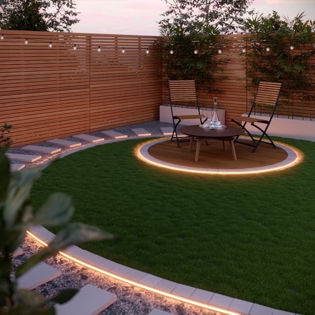 Modern backyard patio with illuminated circular seating area, dining table, two chairs, artificial turf, wooden fence, and LED pathway lighting