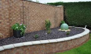 Curved brick garden bed with dark gravel, green plants, and white border edging against brick wall
