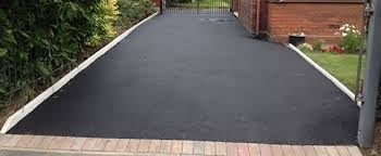 Newly installed dark asphalt driveway with brick border leading to residential home entrance