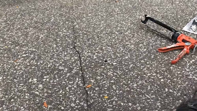 Red and black pipe wrench on asphalt concrete surface with scattered debris