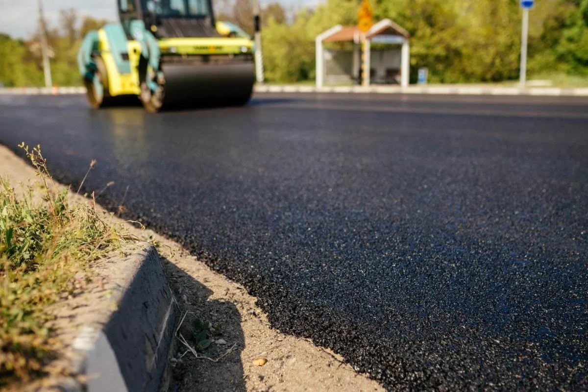 Asphalt roller compacting fresh black pavement on a road construction site with grass edge in foreground