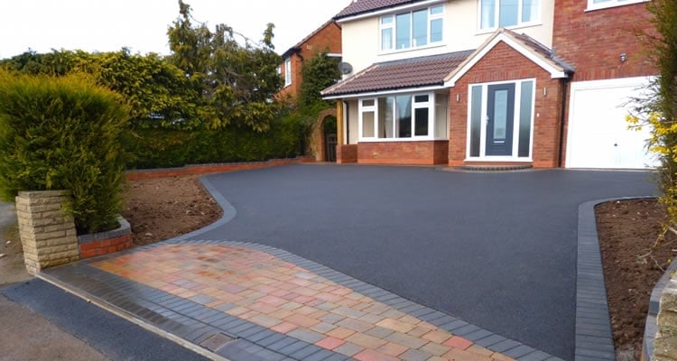 Modern brick house with curved driveway featuring dark asphalt and paved entrance bordered by landscaping