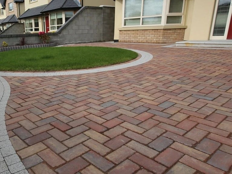 Brick paver driveway with herringbone pattern, curved landscaping, and green lawn, adjacent to residential homes