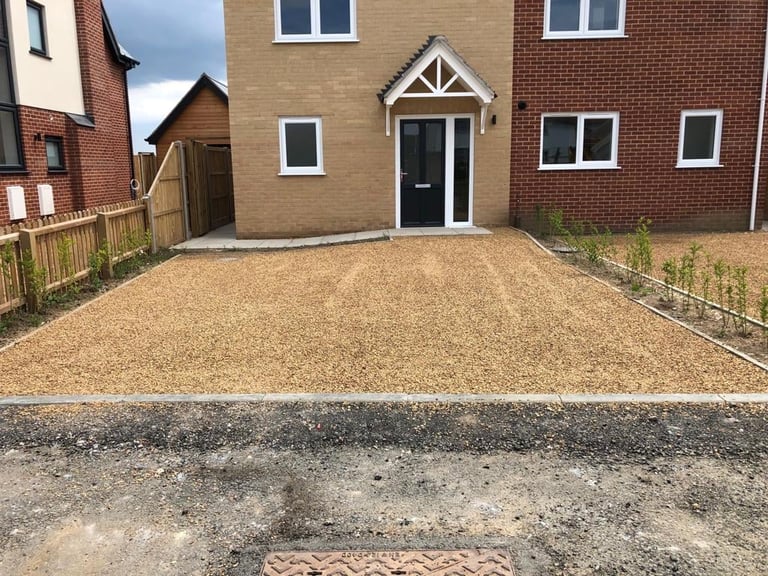 New gravel driveway in front of a modern brick and tan house with black door and white windows