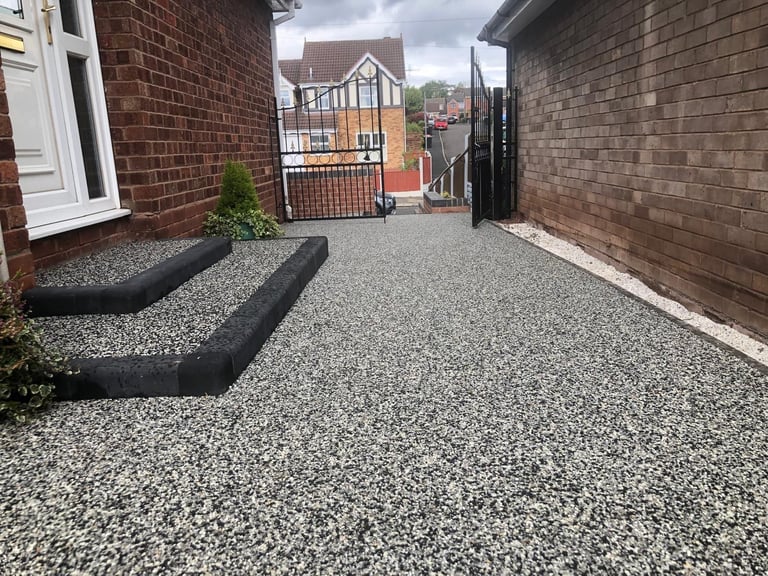 Paved driveway with gravel surface between brick buildings and metal gate in residential area