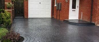 Brick house driveway with white garage door and paved dark surface, showing landscaping and entrance
