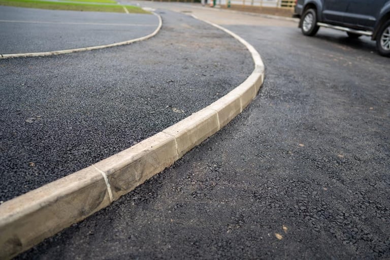 Curved asphalt driveway with concrete edging and parked vehicle visible in background