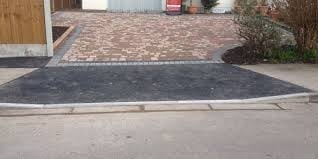 Driveway entrance with dark asphalt apron leading to brick paved surface and wooden garage door