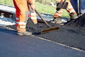 Workers spreading and leveling hot asphalt with tools during road paving construction