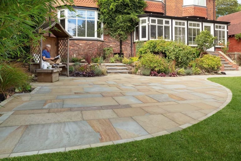 Curved stone patio extending from brick house with green lawn, climbing ivy, and garden plants