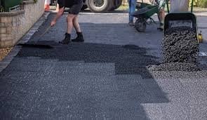 Workers laying asphalt and gravel on a construction site with machinery and tools