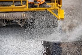 Yellow truck spraying water on asphalt road