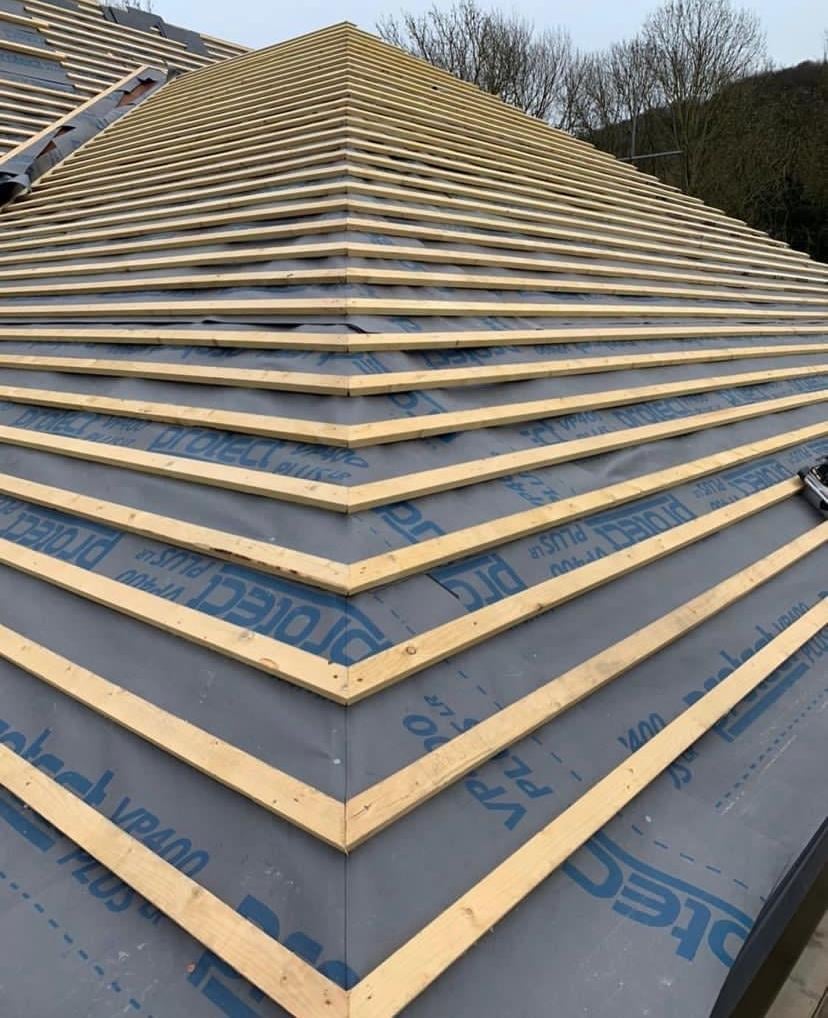 Roof construction showing wooden rafters with blue underlayment and insulation under a pitched roof frame